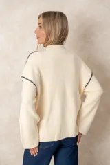 Buzo de punto acanalado color beige, con cuello alto, corte oversize y mangas largas. Presenta costuras decorativas en color negro que recorren los hombros y las mangas.