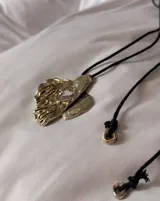 Collar con dije grande de bronce con forma orgánica y textura rugosa, suspendido de un cordón negro. Incluye cordones intercambiables.