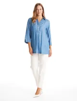 Blusa de lyocell color azul, con cuello camisero, escote en V con cierre de botones y mangas tres cuartos amplias. Presenta un corte holgado con tajos laterales en el ruedo.