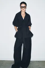 Pantalón de tiro medio con diseño wide leg, confeccionado en mezcla de lyocell. Presenta pinzas en el delantero y cierre frontal con cremallera, botón y ganchos metálicos.
