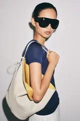 Bolso de hombro de piel en color blanco, con diseño tipo bucket, asa fija y detalle de tira colgante con nudo en el lateral.