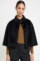 Chaqueta tipo capa de color negro, con cuello redondo y cierre frontal mediante botones grandes. Presenta un diseño minimalista y elegante con corte holgado.