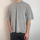 Remera de corte boxy fit con efecto lavado tipo snow wash, color gris. Presenta un diseño lineal bordado en la espalda con forma ovalada.