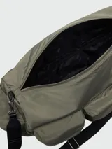 Bolso tipo duffle o bolso de viaje de color verde militar, con múltiples bolsillos exteriores con tapa y correa ajustable de tela negra con detalles en cuero sintético negro.