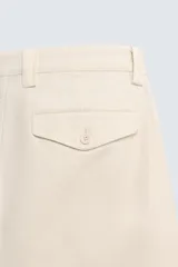 Pantalón relaxed fit color beige confeccionado en tejido de algodón con tacto suave, cintura con pliegues delanteros y cierre frontal con cremallera y botón.