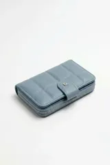 Billetera pequeña de cuero sintético color marrón, con diseño acolchado, cierre perimetral y tira con broche y detalle metálico.