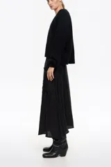 Falda midi de color negro con corte en línea A y diseño con vuelo. Presenta bolsillos plastrón delanteros y cintura ajustable con cordón. Confeccionada en tejido con textura de mezcla de viscosa y lyocell.