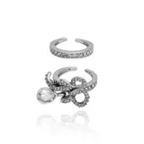 Set de dos anillos con acabado en plata envejecida. Uno de ellos es una alianza simple decorada con cristales engastados, mientras que el otro presenta un diseño intrincado con forma de lazo o infinito cubierto de cristales y un dije colgante en forma de gota con un cristal central.