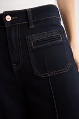 Pantalón de jean azul oscuro con corte flare, tiro alto y bolsillos delanteros tipo plaqué. Presenta costuras a la vista y una silueta amplia en las piernas.