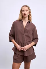 Camisa marrón de manga 3/4, con cuello clásico, botones frontales y un bolsillo en el pecho.