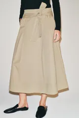 Falda midi color beige confeccionada en hilatura con mezcla de algodón. Presenta tiro medio, cintura con trabillas, bolsillos laterales ocultos en costura y cinturón del mismo tejido. Su diseño incluye un bajo acabado en línea evasé y cierre lateral con cremallera.