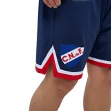 Short de fútbol Umbro del Club Nacional de Football, de color azul marino con detalles en blanco y rojo en los dobladillos. Cuenta con el escudo del club en una pierna y el logo de Umbro junto al número 22 en la otra.