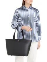 Cartera Tommy Hilfiger tipo tote color negro, confeccionada en poliuretano con acabado liso. Tiene doble asa superior, compartimento principal con cierre de cremallera y logo de metal en la parte delantera.