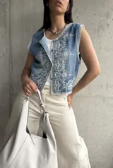 Chaleco de jean celeste con bordado floral blanco, corte recto y cierre frontal con botones.