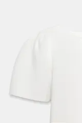 Top de punto blanco con cuello redondo y mangas cortas abullonadas.