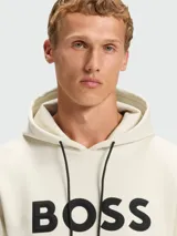 Buzo con capucha Boss modelo Soody Zone, color beige claro, con logo de la marca estampado en negro en el pecho y cordones ajustables en la capucha.