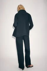 Chaqueta oversize de mezclilla color azul marino, de cuello solapa y manga larga, con bolsillos de parche en el delantero y cierre frontal con botones metálicos.