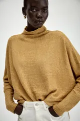 Jersey de punto con textura, color crudo, de cuello subido y manga larga. Presenta un diseño holgado con bajo asimétrico y aberturas laterales.