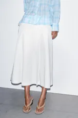 Falda midi de tiro alto en color blanco, con diseño acampanado y detalle de pliegues frontales. Cuenta con cierre lateral mediante cremallera oculta.