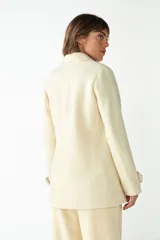 Abrigo de cuello sastre color beige, con forro, cierre frontal con botones, bolsillos con solapa y presillas en mangas. Confeccionado en lana fina sin teñir, diseñado exclusivamente por Don Baez.