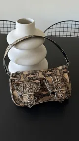 Cartera tipo minibag con estampado de serpiente, correa con aros y dos bolsillos frontales con hebilla.