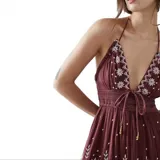 Vestido largo de estilo bohemio en color bordó, con escote profundo tipo halter y espalda descubierta. Presenta detalles de bordados florales blancos en el pecho y a lo largo de la falda, con diseño de paneles escalonados y cintura ajustada.