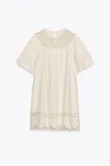 Vestido corto color crudo confeccionado en hilatura con mezcla de algodón y lino. Presenta cuello redondo, manga corta abullonada, detalle de bordados a tono y bajo recto. Cierre en espalda con abertura y botón.