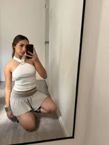 Top color crema con escote halter cruzado y detalle de argolla metálica plateada en el centro del cuello.