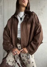 Campera tipo bomber de gamuza color chocolate, con diseño oversize, mangas amplias y apliques decorativos en los hombros. Cuenta con cierre frontal y forro interior.