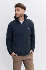 Sweater de punto acanalado en color marrón oscuro, con cuello alto y cierre frontal de cremallera parcial. Presenta mangas largas y puños ajustados.