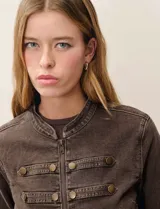 Chaqueta estilo militar de denim color marrón, con cuello redondo, cierre frontal y detalle de botones decorativos en el frente y en los puños.
