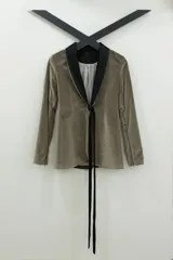 Blazer tipo smoking de terciopelo negro con acabado brillante y detalles estampados en dorado. Presenta solapas clásicas, cierre frontal cruzado mediante un lazo y mangas largas con cierres incorporados. El diseño es entallado y sofisticado.