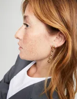 Par de aros colgantes dorados con eslabones de metal con forma de bolitas unidas entre sí.