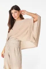Blusa tejida color beige con destellos metalizados, escote bote y mangas anchas y holgadas de tipo murciélago.