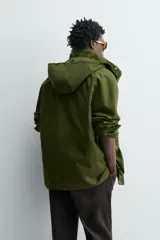 Parka técnica color verde militar de corte relaxed fit con cuello subido y capucha desmontable. Cuenta con bolsillos con solapa en el pecho y en la cadera, cintura ajustable con cordón y cierre frontal de cremallera oculta por solapa con botones a presión. Incluye un chaleco interior desmontable acolchado.