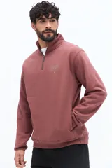 Buzo de algodón color terracota, con cuello alto y cierre parcial frontal. Presenta puños y cintura ajustados, bolsillos laterales y un pequeño logo bordado en el pecho.