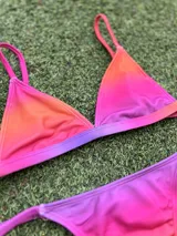 Conjunto de bikini con corpiño triangular fijo y bombacha colaless regulable, con estampado degradado en tonos naranja, rosado y violeta.