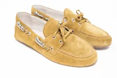 Mocasín de cuero gamuzado color pistacho, con detalle de cordones decorativos y argollas metálicas plateadas en los laterales. Presenta un lazo frontal y suela plana.