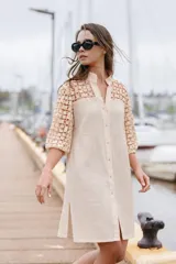 Vestido camisero midi de lino color beige, con cuello mao, cierre frontal abotonado y detalles de tejido crochet en la parte superior y en las mangas de longitud 3/4. Cuenta con aberturas laterales en el dobladillo.