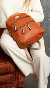 Mochila de cuero sintético en color beige con detalles en color suela. Cuenta con múltiples compartimentos frontales con cierre metálico, correas regulables y manija superior.