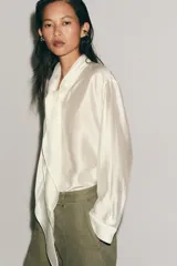 Camisa de tejido satinado con mezcla de lyocell, cuello redondo con escote en pico y lazada frontal. Presenta mangas largas con puños anchos y bajo recto.