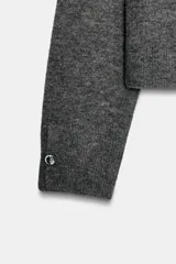Jersey de punto suave con cuello en V y manga larga, con detalle de botones metálicos en los puños.