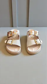 Sandalias planas de cuero color blanco, con dos tiras anchas ajustables mediante hebillas metálicas doradas y detalles pintados a mano en tonos multicolores.