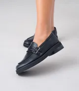 Mocasín de cuero vacuno negro con detalle de pieza de cuero con textura de cocodrilo y hebillas metálicas. Suela de caucho con plataforma.
