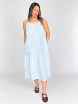 Vestido midi celeste de silueta amplia y fluida, con escote fruncido y tirantes finos decorados con cuentas de madera. Incluye una pequeña carterita colgante haciendo juego.