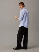 Camisa de manga larga Calvin Klein confeccionada en popelina de algodón elástico con diseño de rayas verticales. Presenta cuello en punta, cierre frontal de botones, bolsillo de parche en el pecho con logo bordado y bajo redondeado.