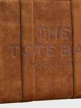 Bolso tote grande Marc Jacobs, modelo The Suede Leather Blocked Large Tote. Cuerpo principal de gamuza color camel con texto en relieve y detalles laterales y base en cuero marrón oscuro.