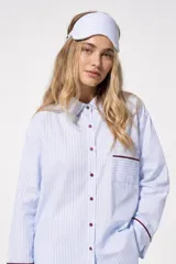 Pijama de dos piezas de algodón a rayas celestes y blancas, compuesto por una camisa de manga larga con botones y ribetes marrones, y un pantalón largo de corte recto con elástico en la cintura.