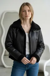 Campera tipo aviador de cuero sintético negro con interior y cuello de corderito sintético negro. Presenta cierre frontal, hebillas metálicas en el cuello y puños con terminación en corderito.