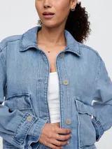 Campera de jean en tono azul claro, con diseño utility que incluye bolsillos frontales con solapa, cierre frontal con botones y puños ajustables con botón.